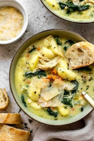 Dipping baguette into a bowl of creamy chicken gnocchi soup with spinach.