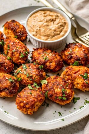 Fresh salmon croquettes made with mashed potatoes on a plate with dipping sauce.
