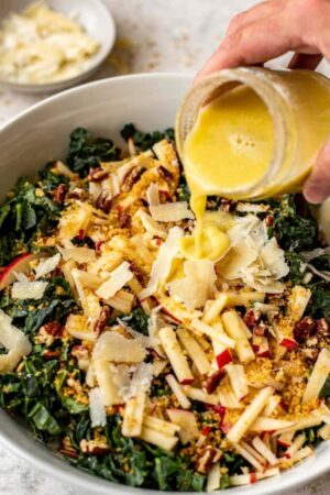 Pouring lemon tahini dressing on kale salad.
