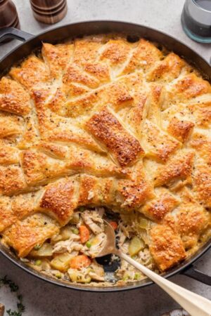 Slice removed from golden brown chicken pot pie in puff pastry.