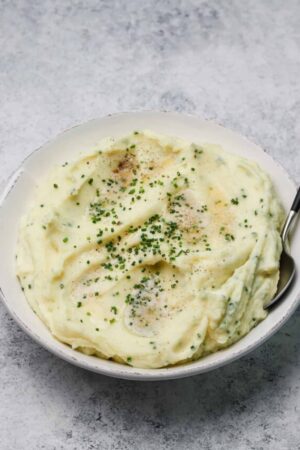 Sour cream mashed potatoes in a bowl with fresh chives and a spoon.