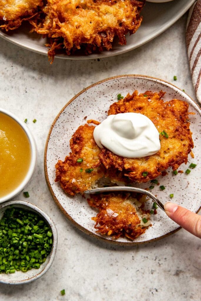 Crispy fried latkes with sour cream on a plate, sprinkled with chives.