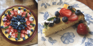 An Italian ricotta cheesecake topped with strawberries, blueberries, mint leaves, and edible flowers. Next to it is a slice of the same cake on a floral-patterned plate, garnished with similar fruit and flowers.