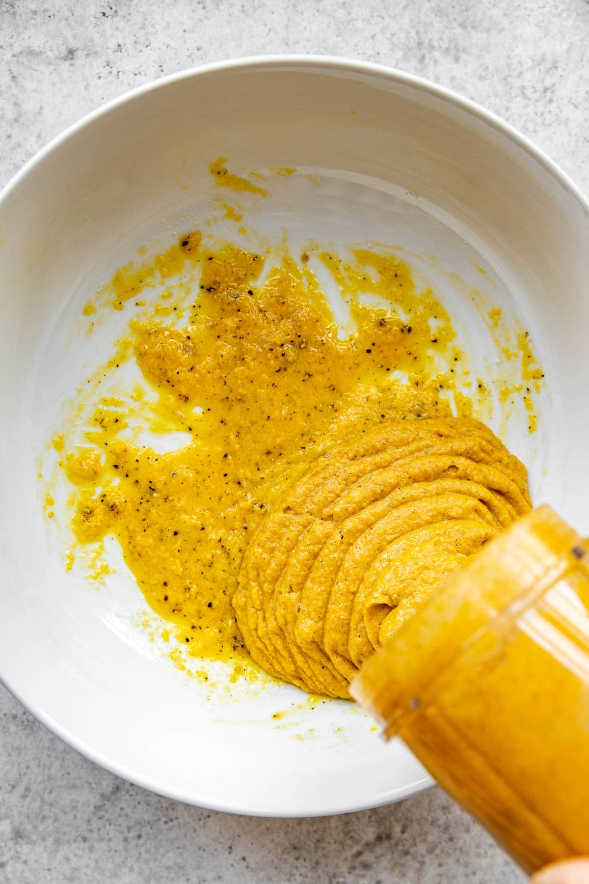 Adding butternut squash purée to a mixing bowl for carbonara pasta.