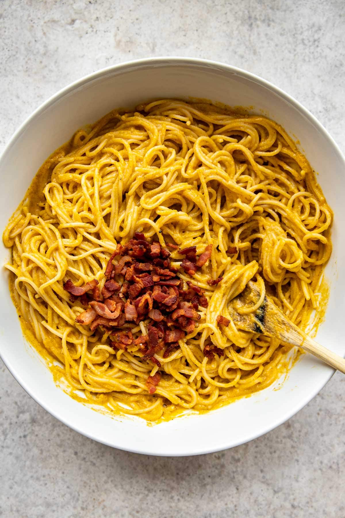 Adding crispy bacon to a bowl of pasta.