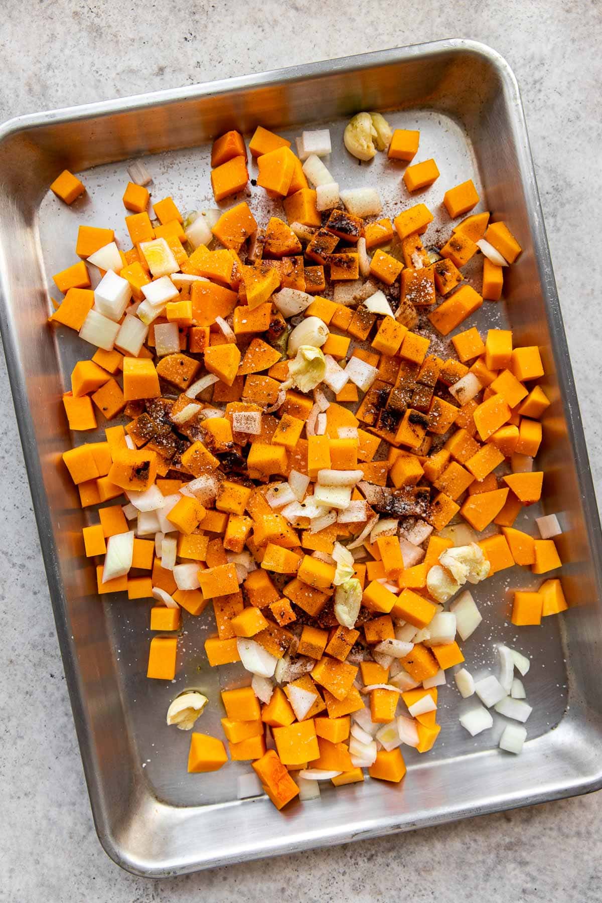 Cubed butternut squash with onions and spices on a baking sheet.