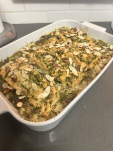 An oven baked salmon casserole with fillets topped with herbs and sliced almonds, served over seasoned rice. The dish sits on a gray countertop with a white subway tile backsplash in the background.