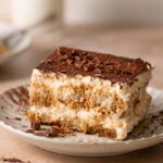 Italian tiramisu on a plate with cocoa powder and chocolate shavings.