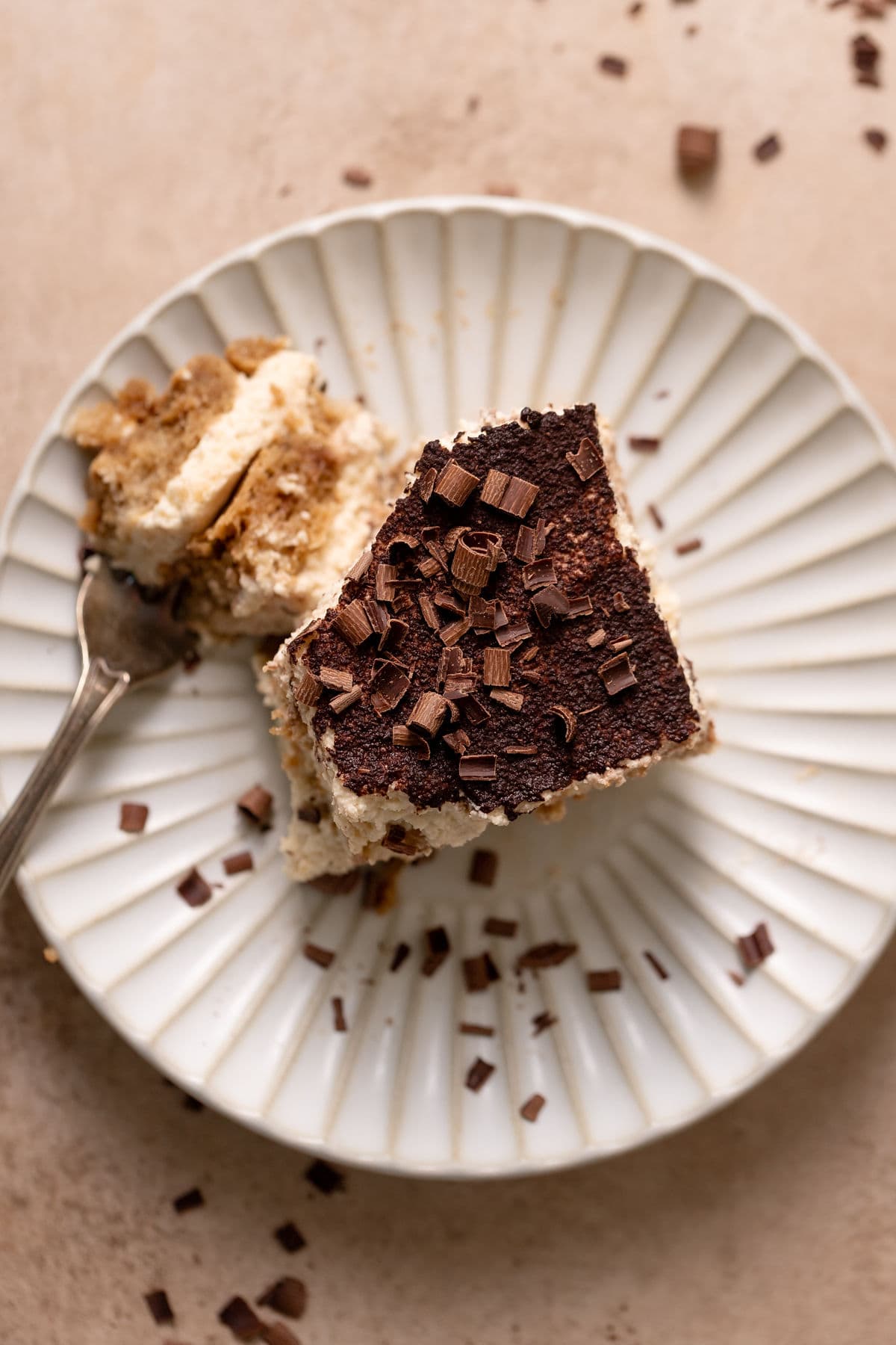 Slice of tiramisu on a plate with chocolate shavings on top and a fork on the side with a bit of tiramisu on it.