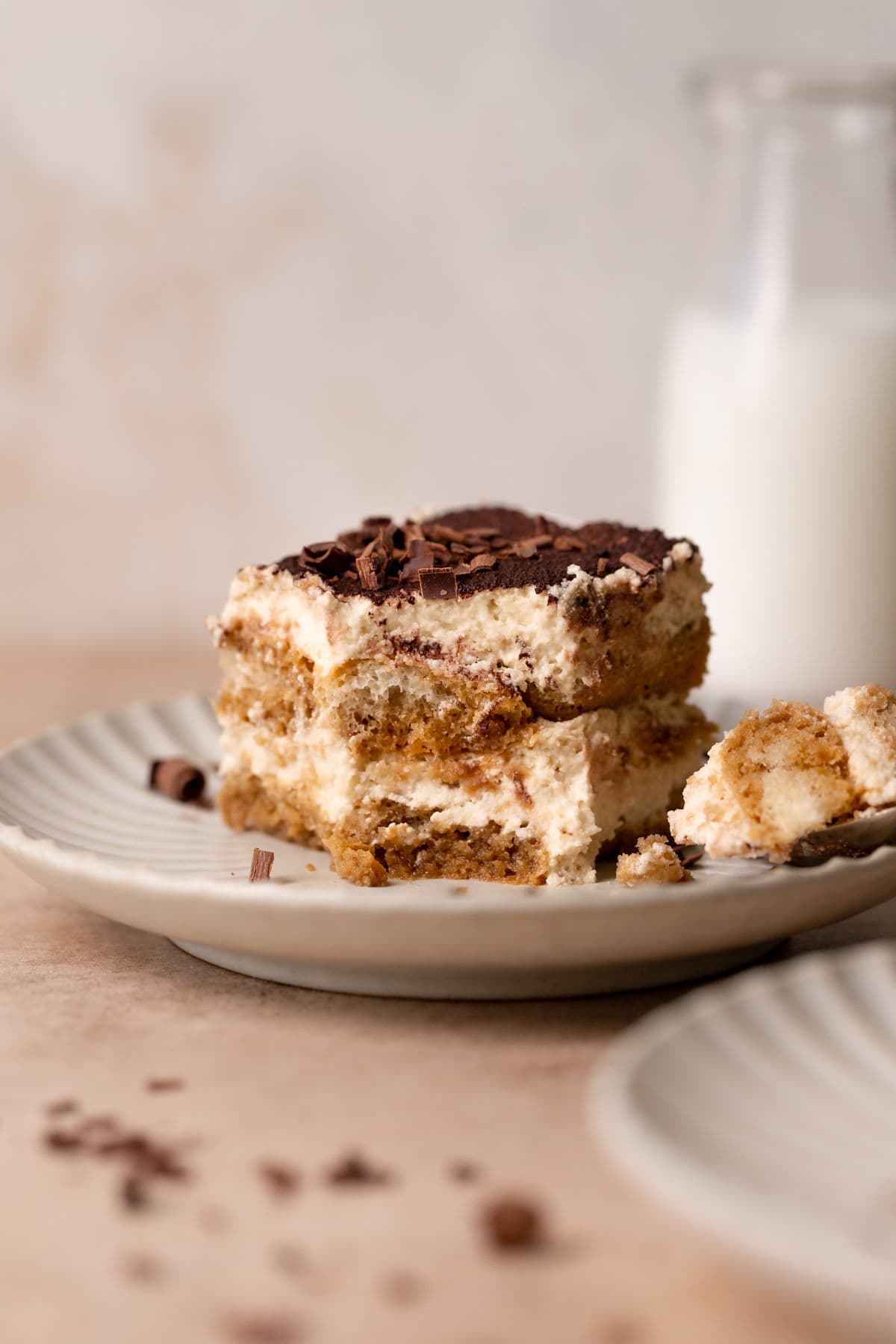 Tiramisu with a bite taken out of it on a plate with a glass of milk on the side.