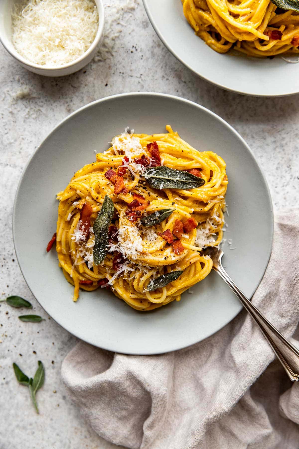 Two plates of butternut squash pasta with crispy sage leaves and bacon.
