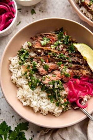 Skirt steak over rice with chimichurri sauce, lime wedges, and pickled red onion.