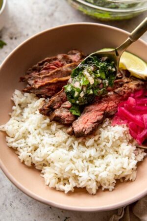 Spooning chimichurri sauce onto steak rice bowls.