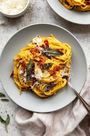 Two plates of butternut squash pasta with crispy sage leaves and bacon.