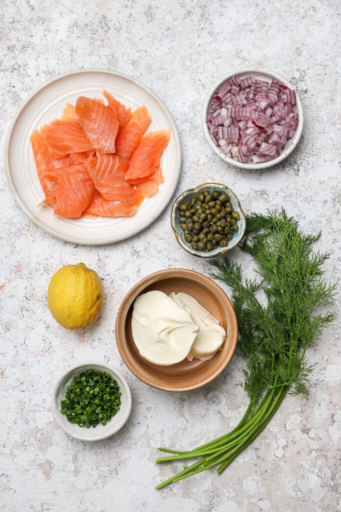 A flat-lay view of premium ingredients including smoked salmon, crème fraîche, and herbs prepared for a crispy potato galette topping.