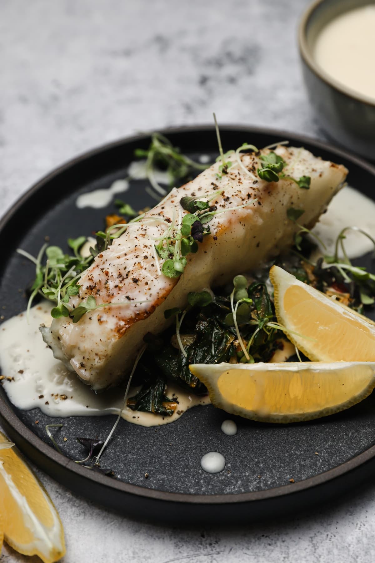 Pan seared chilean sea bass with lemon beurre blanc on a black plate.