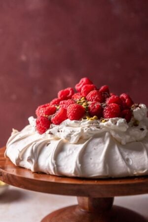 Pavlova on a cake stand with raspberries chocolate and pistachios.
