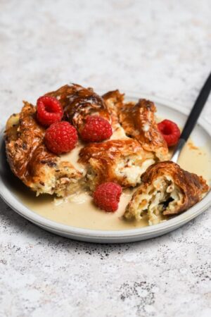 Slice of bread pudding on a plate with raspberries and creme anglaise.