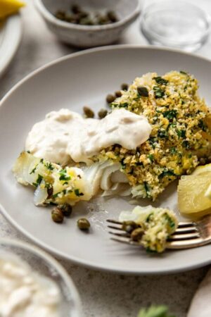 Flaky parmesan crusted cod with tartar sauce on a plate.