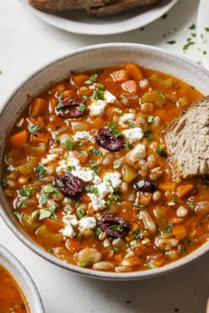 Greek white bean soup in a bowl with kalamata olives and feta cheese.