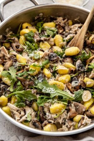 Potato gnocchi with mushrooms chicken and arugula in a pan.