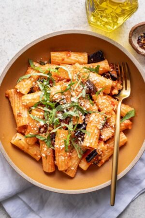 A bowl of eggplant pasta with basil and red sauce.