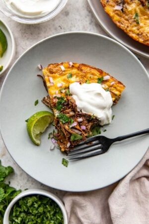 Slice of birria frittata with sour cream cilantro and red onion on a plate.