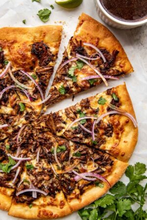 Sliced braised beef pizza with red onion cilantro and birria consomme on the side.