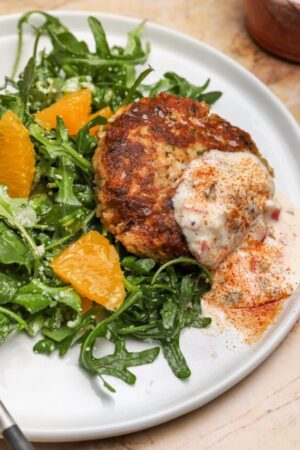 Maryland crab cake with tartar sauce on an arugula salad with orange segments.