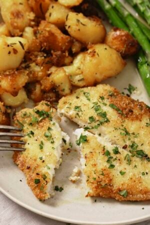 Pan fried sole meuniere with parsley on a plate with roasted potatoes and steamed asparagus.
