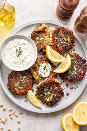 Fresh zucchini fritters on a plate with Greek yogurt sauce.