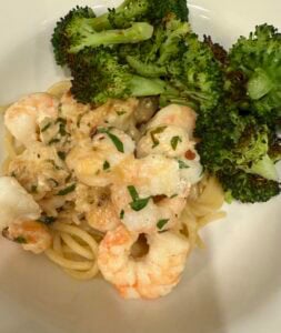 A plate of pasta topped with shrimp scampi in a creamy sauce, garnished with herbs, served alongside roasted broccoli florets.