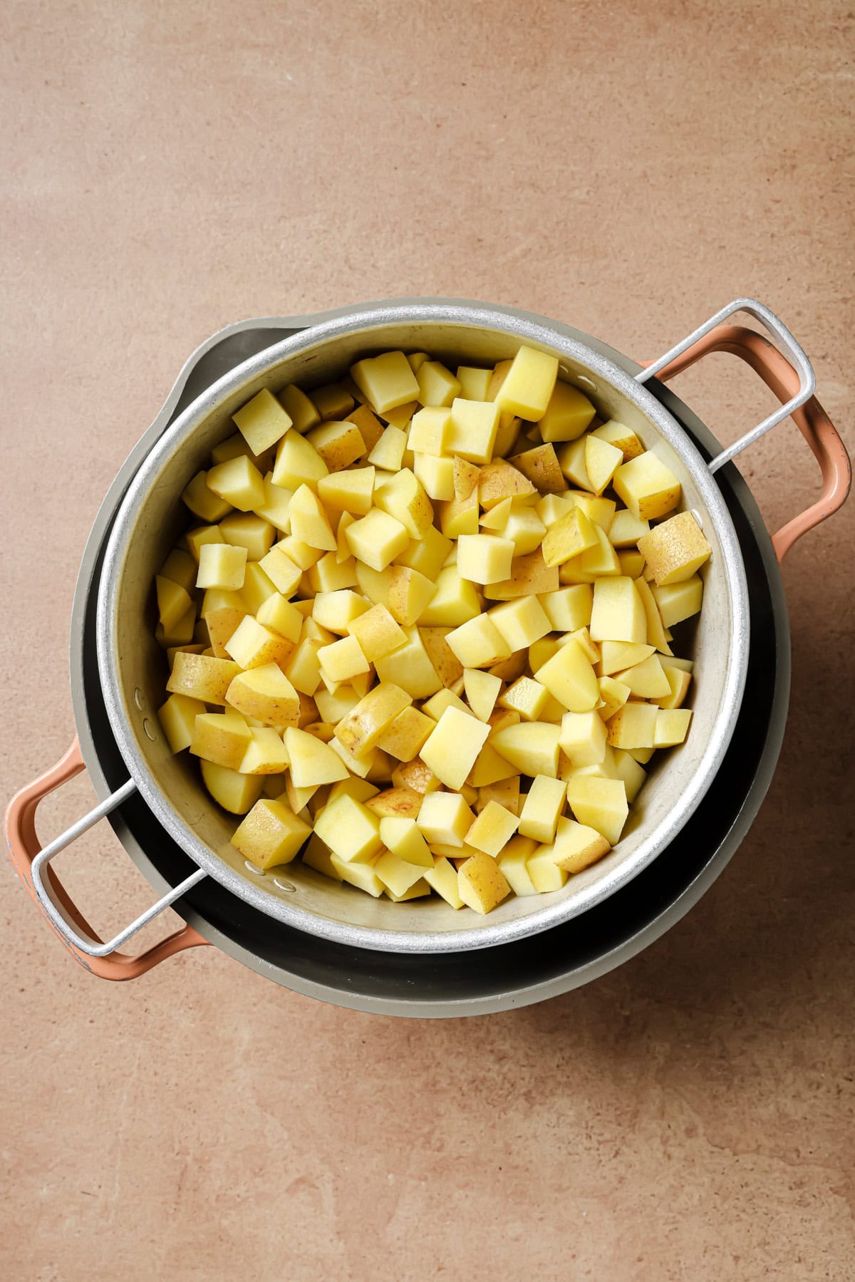 A pot filled with diced yellow potatoes sits atop another pot on a brown countertop, ready for cooking.