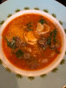 A bowl of cheesy tortellini soup with ground meat and spinach in a tomato base, topped with grated cheese.