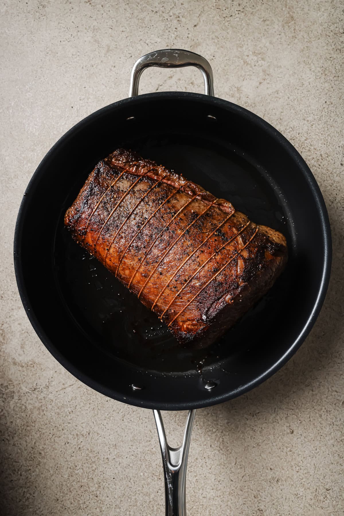 A browned, tied roast sits in a black skillet on a light-colored countertop, ready for further cooking.