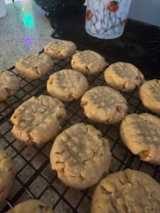 Freshly baked peanut butter cookies with sugar sprinkles cool on a wire rack atop the kitchen counter. A decorative cup and black surface add charm to the background scene.