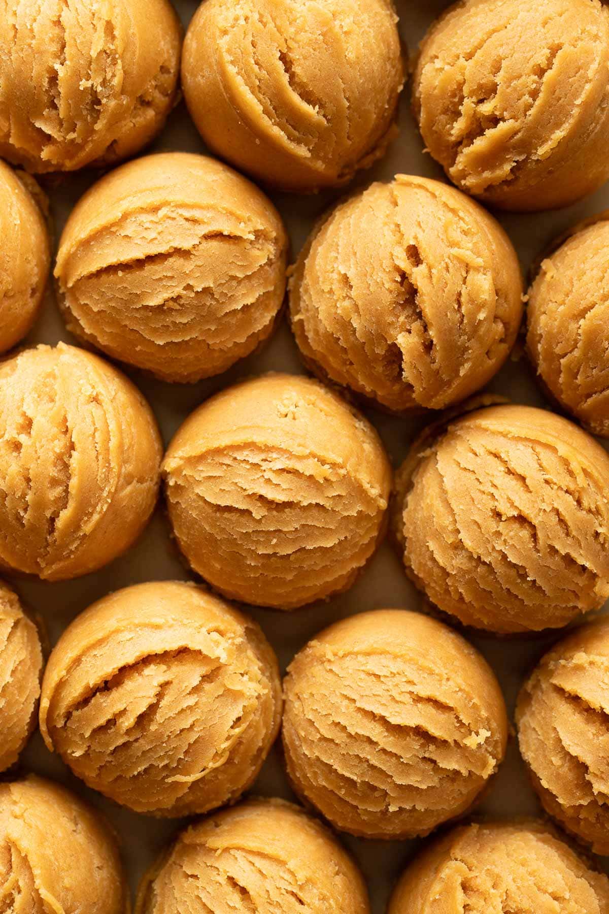 Rows of evenly spaced, round scoops of peanut butter cookie dough are arranged closely together, showing a smooth, creamy texture with visible swirl marks from a cookie scoop.