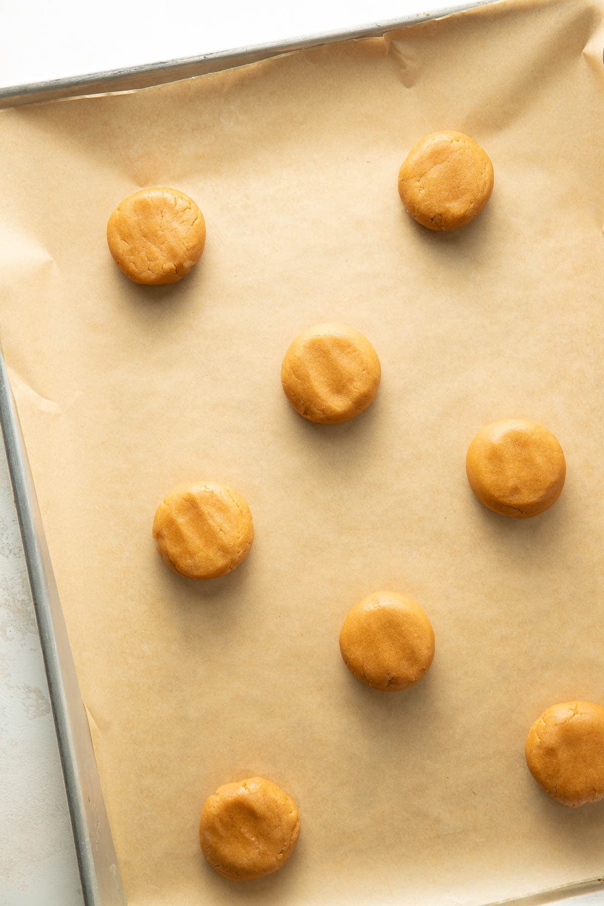 A baking sheet lined with parchment paper holds nine evenly spaced, round, unbaked cookie dough balls ready for baking.