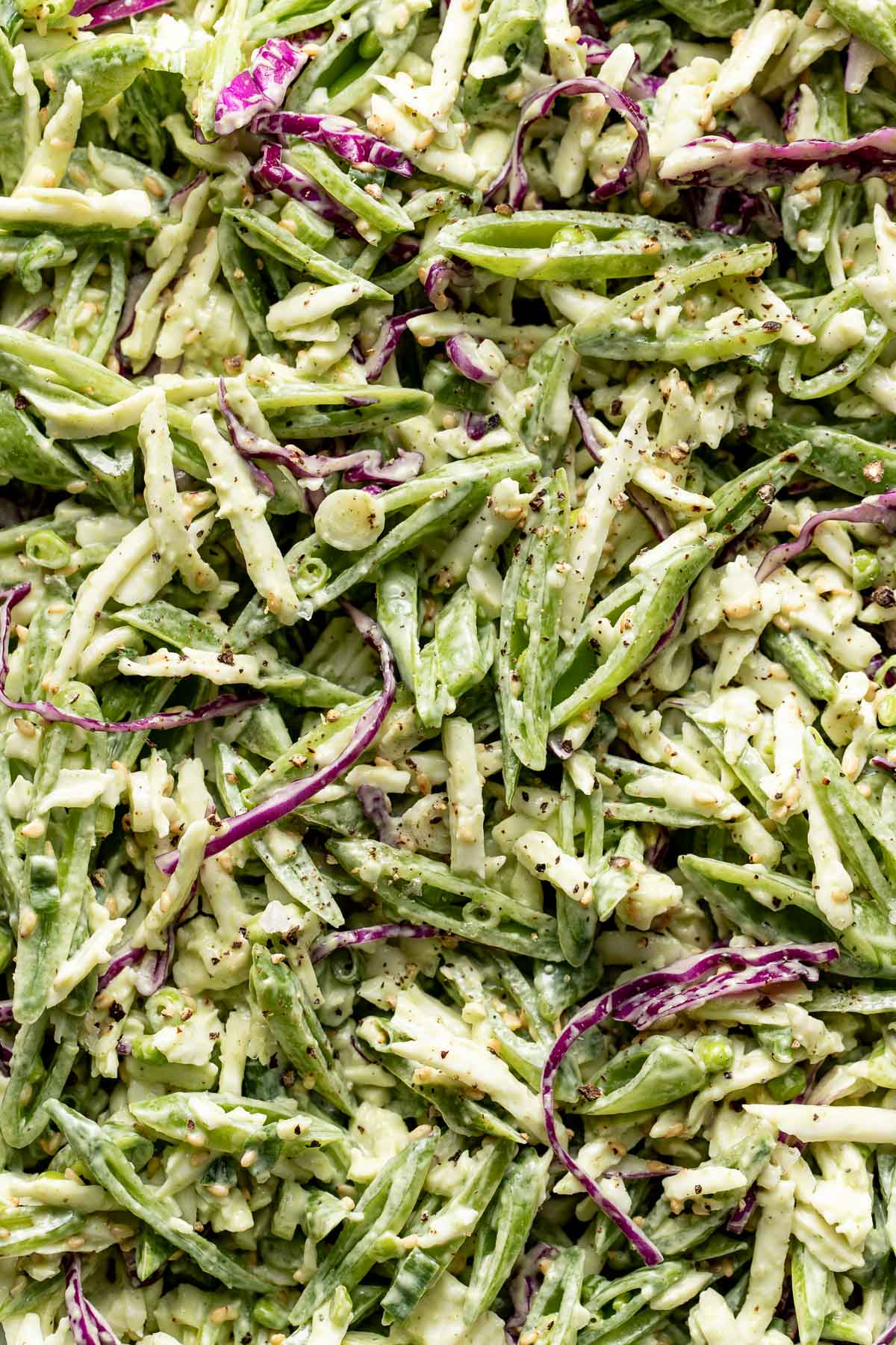 Close-up of a fresh salad with green beans, shredded cabbage, and purple cabbage strips, all coated in a creamy dressing and topped with cracked black pepper.