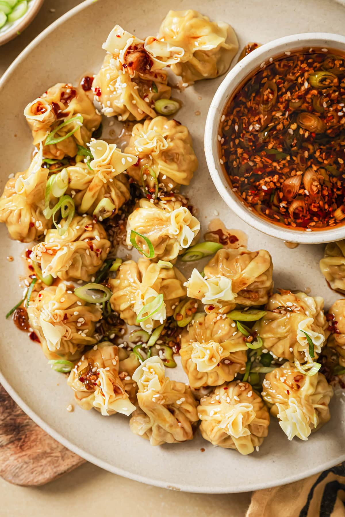 A plate of steamed dumplings garnished with sliced green onions and sesame seeds, served with a bowl of spicy dipping sauce on the side.