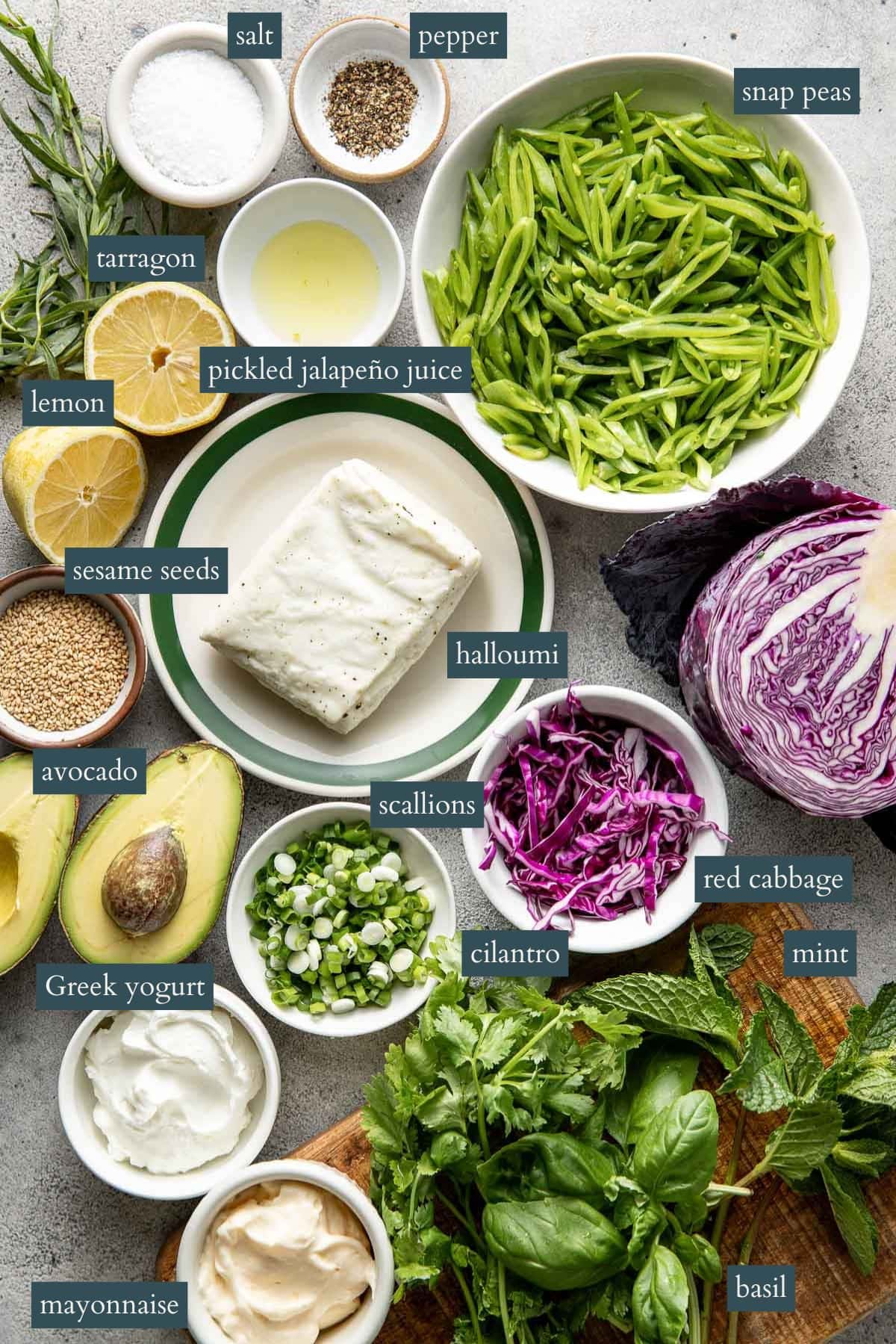 A top view of various fresh ingredients labeled, including snap peas, red cabbage, scallions, avocado, halloumi, Greek yogurt, mayonnaise, basil, mint, cilantro, lemon, tarragon, salt, pepper, sesame seeds, and pickled jalapeño juice.