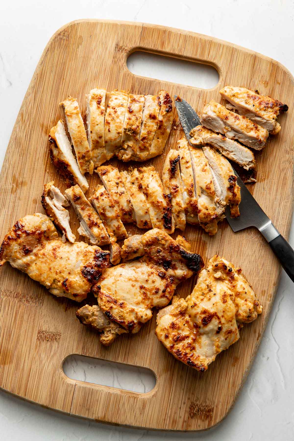 Sliced, grilled chicken breasts on a wooden cutting board with a knife, showing juicy, browned pieces ready to serve.