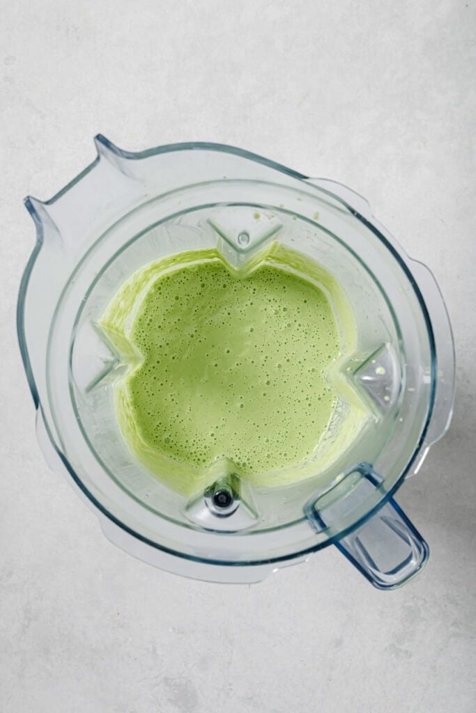 A top-down view of a blender containing a light green, frothy liquid, set on a light gray surface.