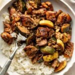 A bowl of white rice topped with sautéed chicken, zucchini, and yellow squash, seasoned with herbs and spices. A fork rests in the bowl, ready for eating.