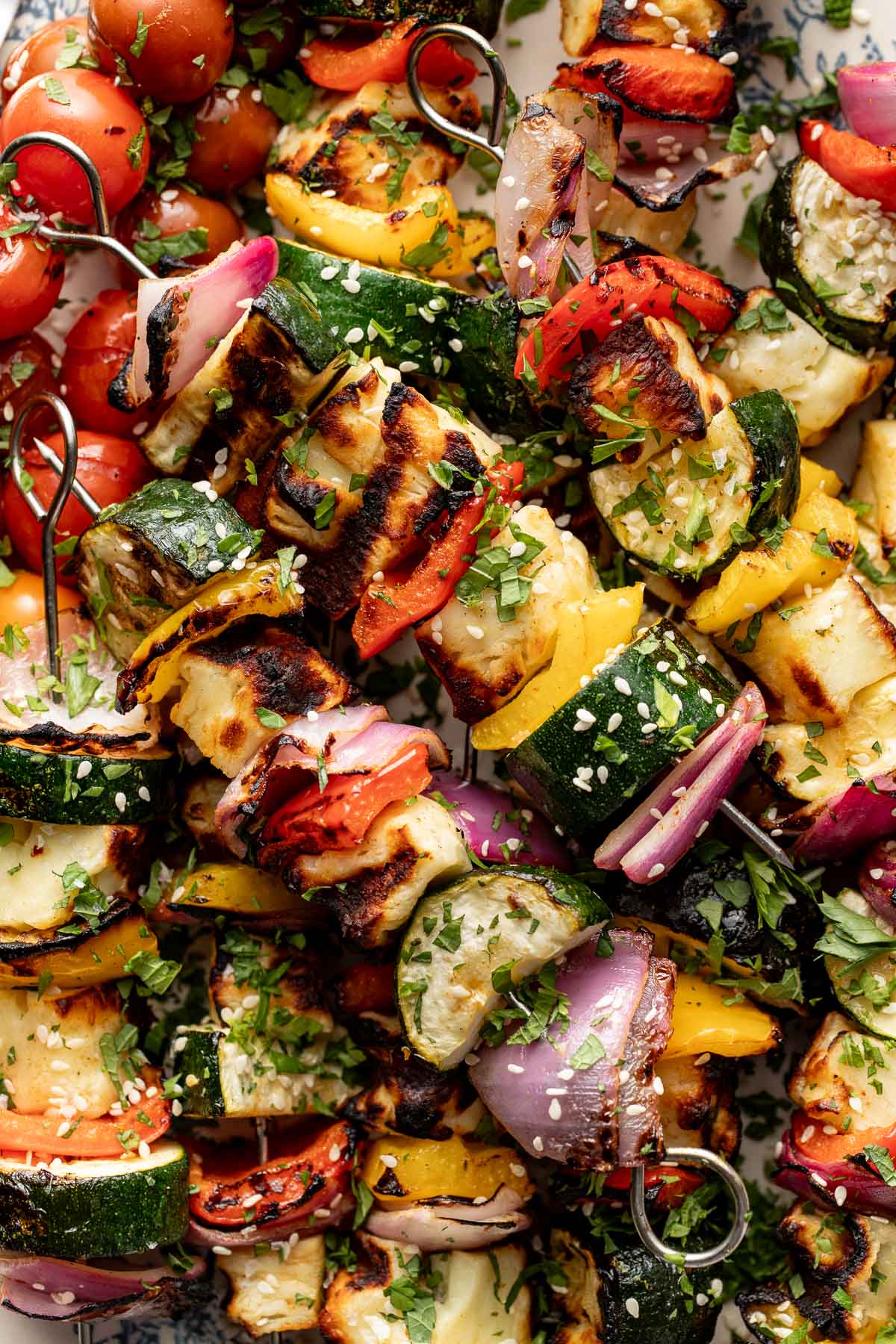 Colorful vegetable skewers with zucchini, red and yellow bell peppers, red onion, tomatoes, and herbs, grilled and sprinkled with sesame seeds and chopped parsley.