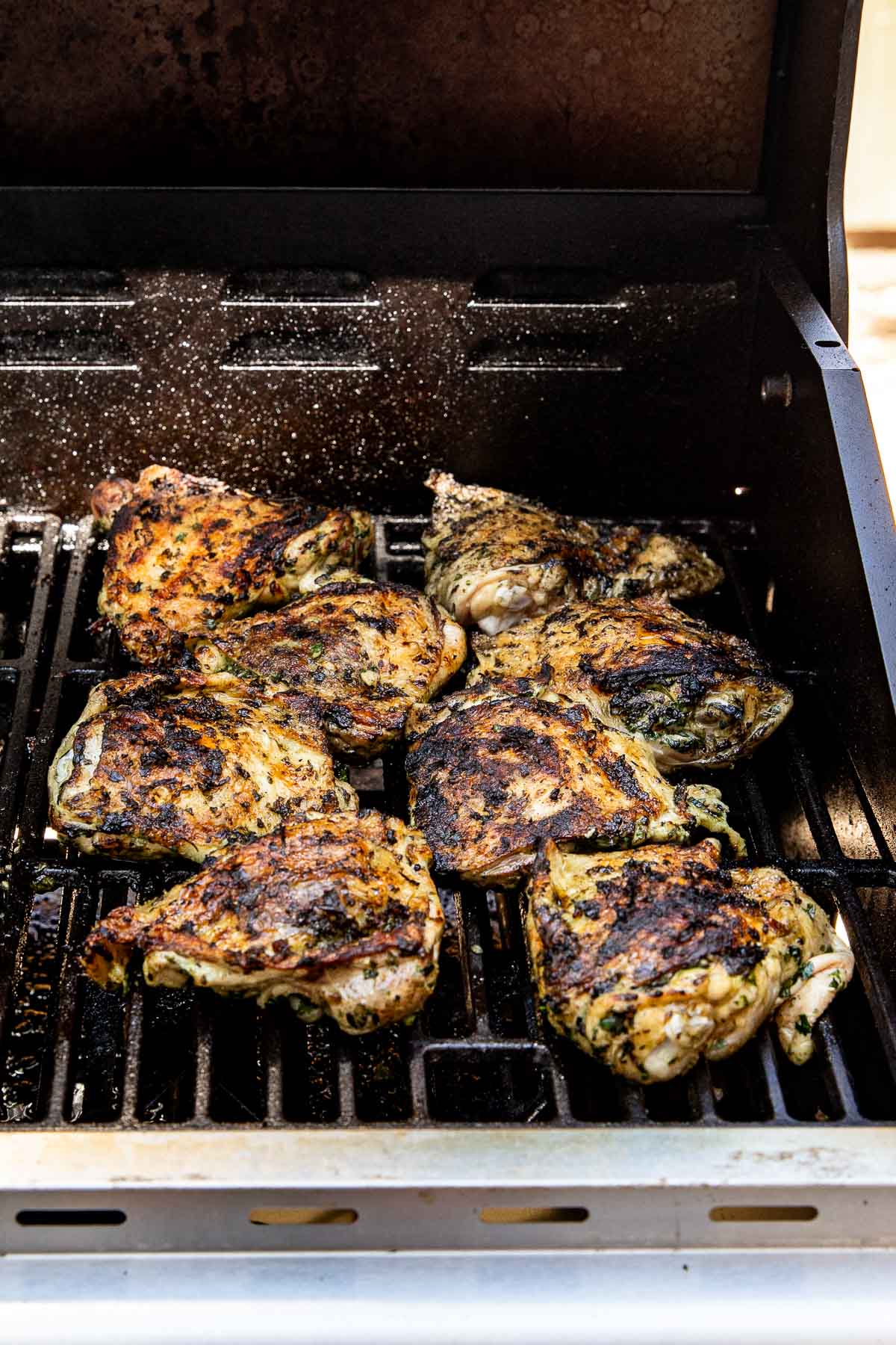 Grilled marinated chicken pieces with char marks cooking on an outdoor barbecue grill, with the grill lid open.