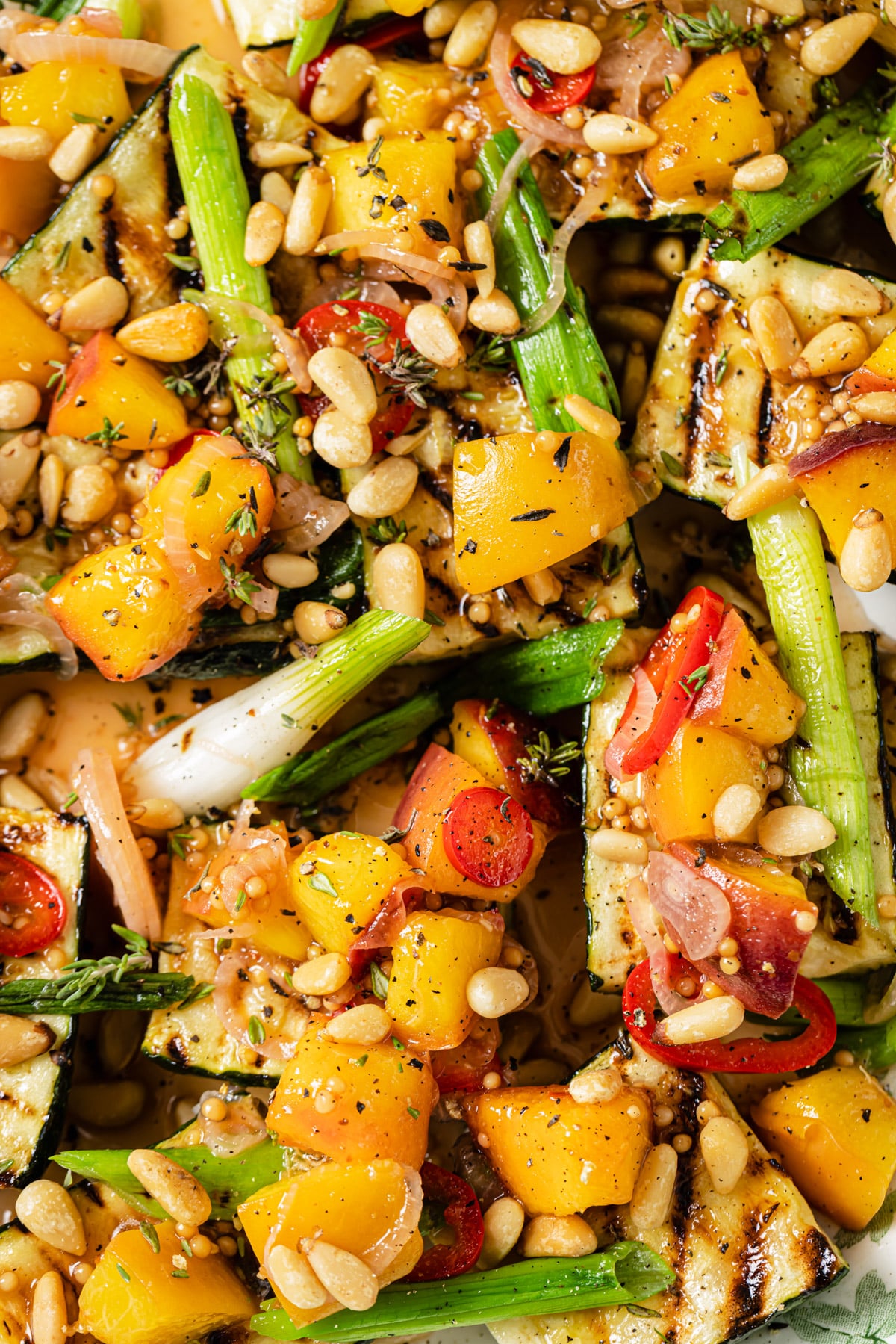 Grilled zucchini and green onions topped with diced yellow peaches, cherry tomatoes, pine nuts, and fresh herbs, all seasoned with black pepper and herbs.