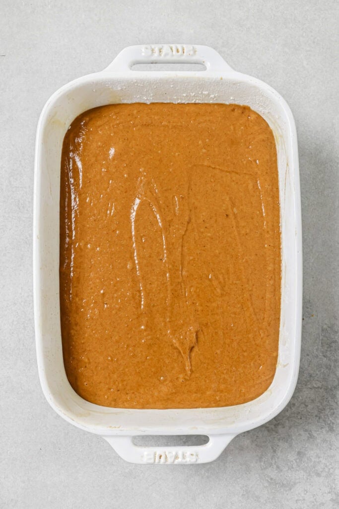 A white rectangular baking dish filled with smooth, light brown cake batter sits on a gray surface, ready to be baked.