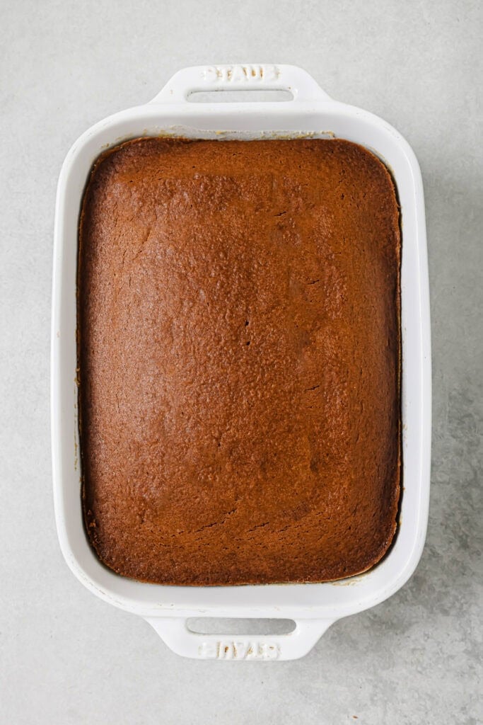 A rectangular, golden-brown cake in a white ceramic baking dish, viewed from above on a light gray surface.