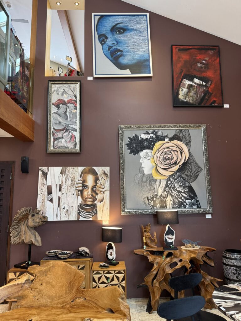 A modern living space with brown walls, decorated with various colorful paintings, wooden furniture, art sculptures, and two table lamps, creating a vibrant and artistic atmosphere.